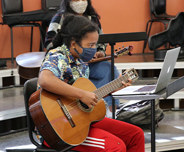 Student playing guitar. Links to Gifts of Life Insurance